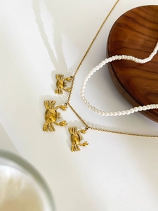 Macro detail of three gold crab charms on a titanium steel necklace with pearl accents