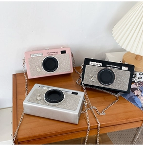 Three rhinestone-embellished camera-shaped cross-body bags in pink, black, and silver colors