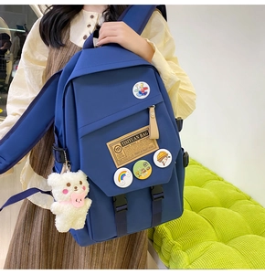Detail of dark blue nylon school backpack featuring cute bear plush charm and cartoon badges