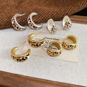 Boucles d'oreilles créoles léopard vintage en or et argent sur fond de tissu tweed