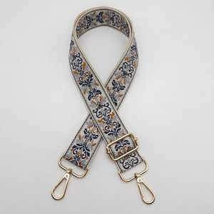 Detail of floral embroidered beige bag strap with blue patterns and gold metal buckles