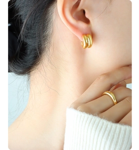 Detail of double C-shaped gold-plated hoop earrings and minimalist solitaire ring on model