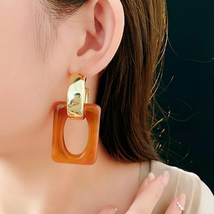 Close-up of geometric C-shaped golden hoop earring with a stylish amber resin pendant