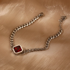 Detail eines silbernen Panzerarmbands mit quadratischem rotem Zirkon auf Seidenstoff