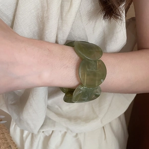 Detailed view of green marbled acrylic resin bangle on model with linen clothing background