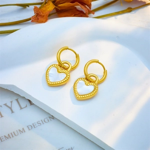 Elegant gold heart earrings with white shell inlay on a decorative plaster tray