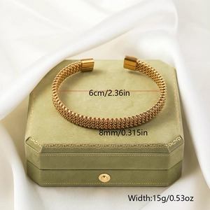 Detail of golden woven twisted bangle with square ends on green jewelry box
