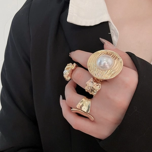 Close-up of gold layered rings set featuring a large pearl and textured metal finish