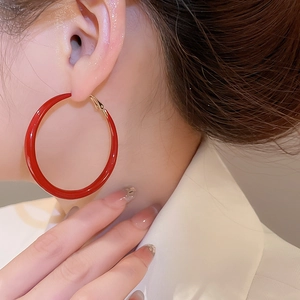Close-up of a model wearing large red enamel hoop earrings with golden metal clasps
