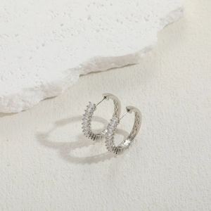 Macro shot of silver round earrings featuring rectangular clear zircons and metal texture