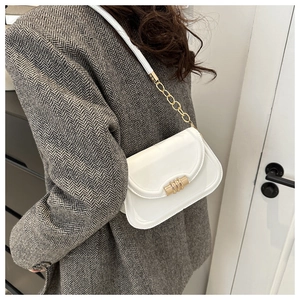 Detail view of a white patent leather crossbody bag with golden chain and hardware buckle