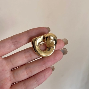 Makroansicht einer goldenen, minimalistischen Anstecknadel mit organischer Form