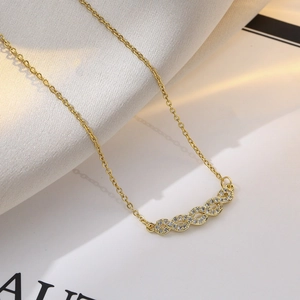 Close-up of a gold heart wave necklace with crystals on soft fabric and paper background