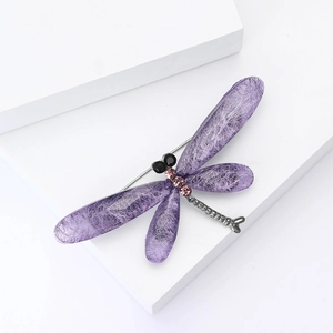 Elegant purple dragonfly brooch with crystal rhinestones on a minimalist white pedestal