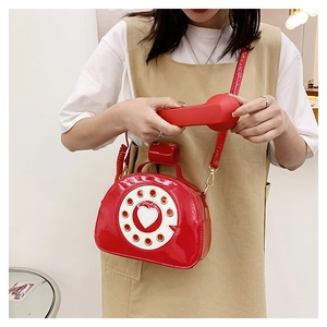 Detail of red patent leather telephone bag showing a heart dial and shiny strap