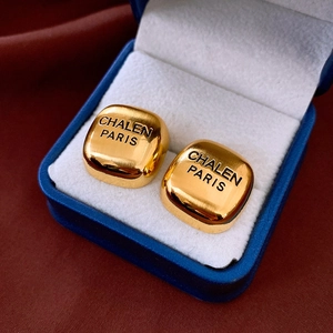 Macro detail of square gold stud earrings with brushed metal texture and engraved lettering