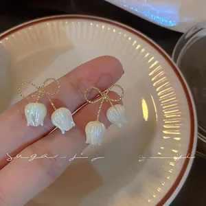 Close-up of elegant lily of the valley earrings with gold bows and white flower petals