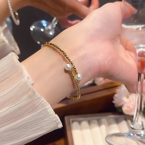 Detail view of a gold beaded bracelet with two white pearls on a woman's wrist