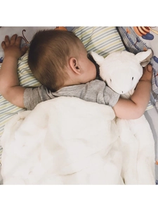 Soft white plush infant security blanket being held by a sleeping baby on patterned sheets