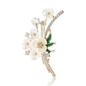 Broche fleur dorée élégante avec pétales en émail blanc, feuilles vertes et cristaux