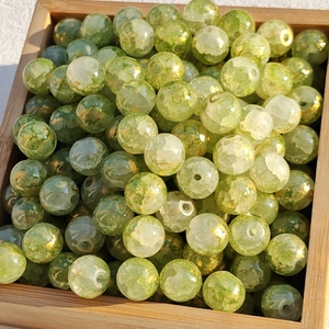 Macro detail of green glass beads with gold foil and cracks in a wooden tray