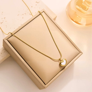 Detail shot of a gold heart necklace with white shell inlay on a beige display stand