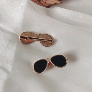 Detail showing two gold sunglasses-shaped hair clips with black lenses on white silk