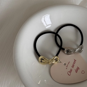 Detail of gold and silver metal bow hair ties on a white ceramic plate with elastic cord