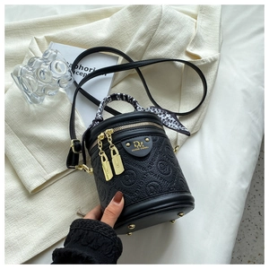Detail of black cylindrical bucket bag with gold hardware and silk scarf handle