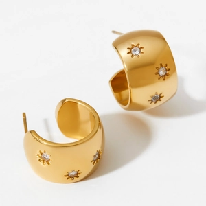 Golden C-shaped hoop earrings with sparkling zircon starbursts on warm white background
