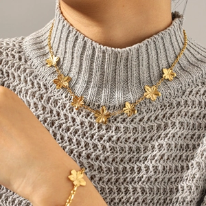 Detailed view of gold flower necklace and bracelet set on a woman wearing a sweater
