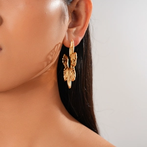 Detail of a large gold hollow floral earring worn on ear with metallic brushed texture