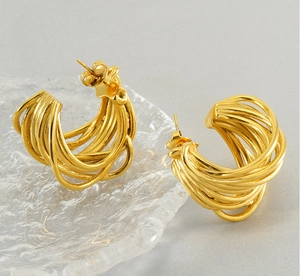 Detail of gold multi-layer twisted hoop earrings on a textured glass surface
