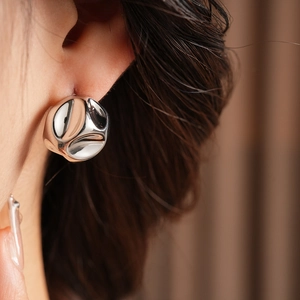 Detailed close-up of a silver spherical earring with unique textured surface on model