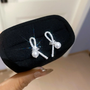 Close-up of silver knotted stud earrings with sparkling rhinestones and white pearls