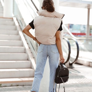 Back view of a beige padded puffer vest with a stand collar in an urban street setting