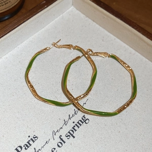 Detail of hammer-textured gold earrings with deep green enamel and wavy organic curves