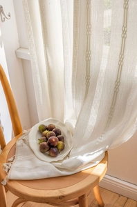 Close-up of cream white textured curtains with diamond weave pattern and tassel detail