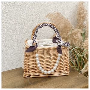 Detailed view of woven straw handbag with houndstooth handle and pearl chain