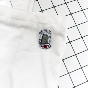 Gothic tombstone enamel pin with Stay In Bed lettering on a white canvas bag background