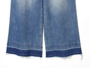 Macro view of raw hem and contrast patchwork stitching on washed blue denim jeans
