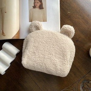 Dettaglio della borsa a forma di orsetto in peluche beige su tavolo di legno