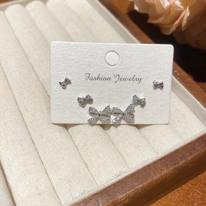 Macro detail of three pairs of silver zircon bow earrings in a beige velvet jewelry box