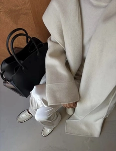 Detail view of cream wool coat fabric texture paired with a black leather tote bag