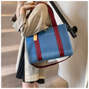 Detail of blue denim tote bag with red striped handles and golden magnetic closure