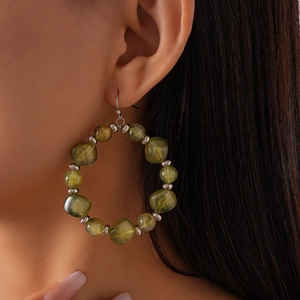 Detail view of large hoop earrings with green acrylic beads and silver spacers on model