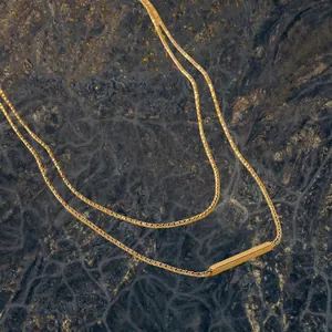 Minimalist double layer T-bar stick necklace in 18K gold finish on black rock surface