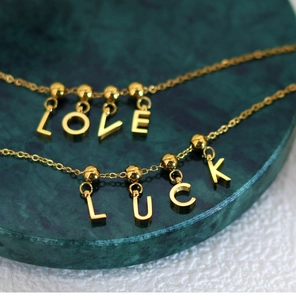 Macro shot of gold necklaces with LOVE and LUCK letter pendants on green marble