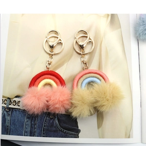 Detail of woven rainbow keychain featuring soft plush pom-poms and golden alloy clasp