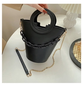 Detail view of black PU leather bucket bag with chunky chain and round handle on white table